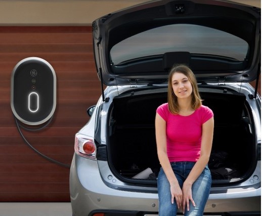 Chica en vehículo eléctrico cargando las baterías en su casa con su punto de carga